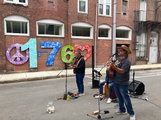 A band performing in an ally, in front of the peace sign 1760 display during Natick Nights