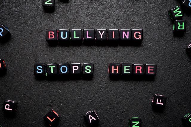 Color graphic with a black background featuring black square beads with different color letters on them. They spell out "Bullying stops here."