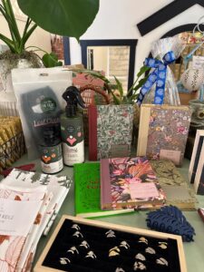 A modern color photograph of a store display. There are rings, journals, plant spray, plants, towels and more.