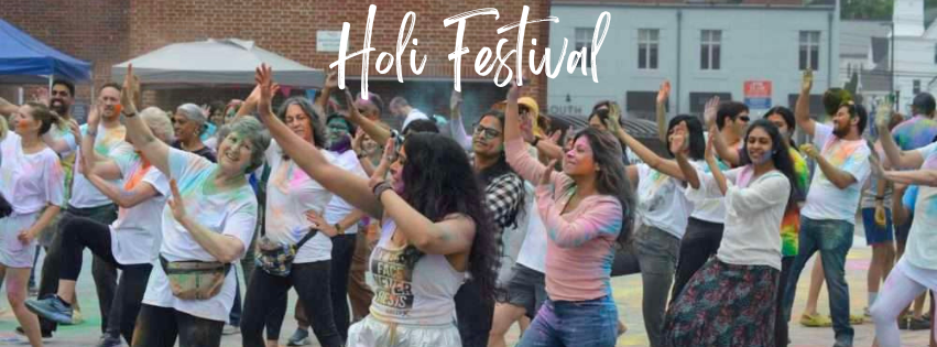 Modern color photograph of many people in white clothes stained with colored powder, all facing towards the camera, mid dance move.
