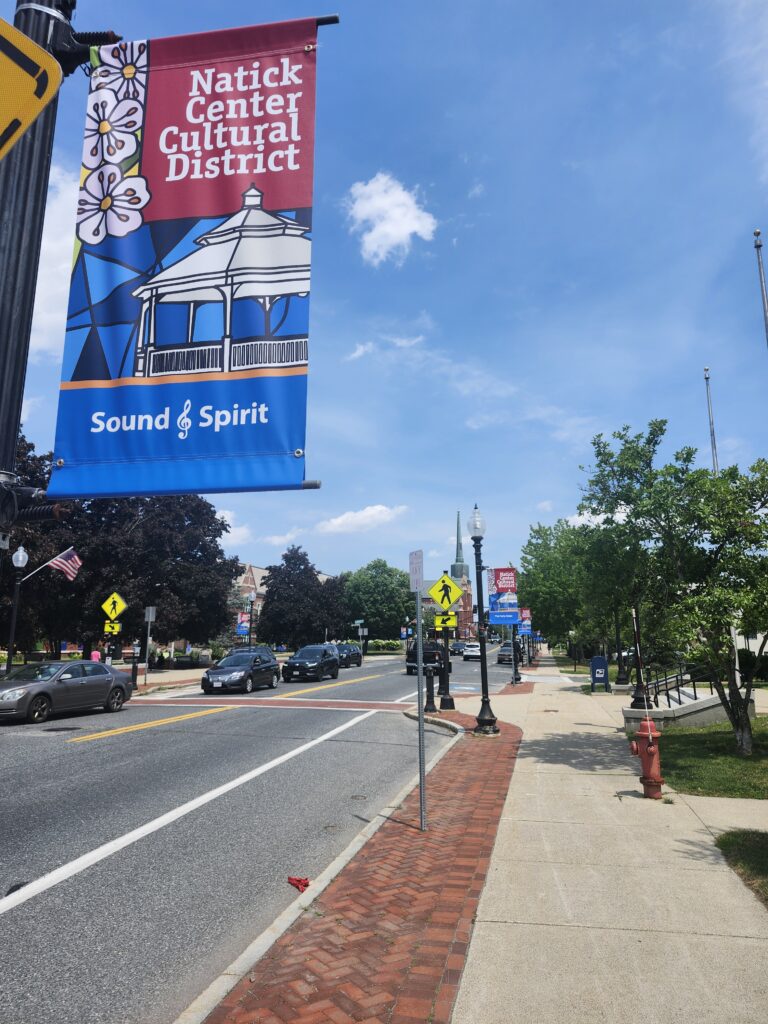 A modern color photograph of an urban scene with brick buildings, cars on the road and a banner on a street pole.